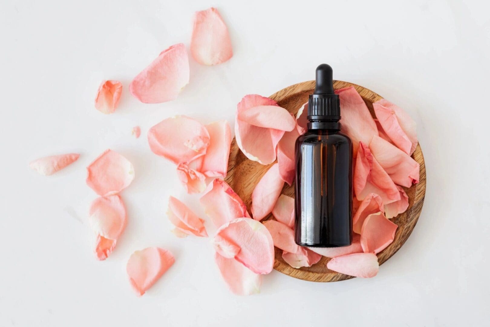 A bottle of essential oil sitting on top of pink petals.